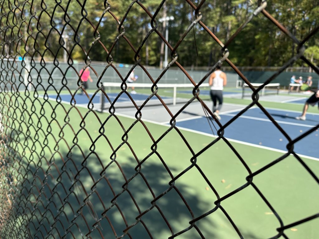 Picture of people between Pickleball points taken through a fence surrounding the pickleball courts at Ephesus Park