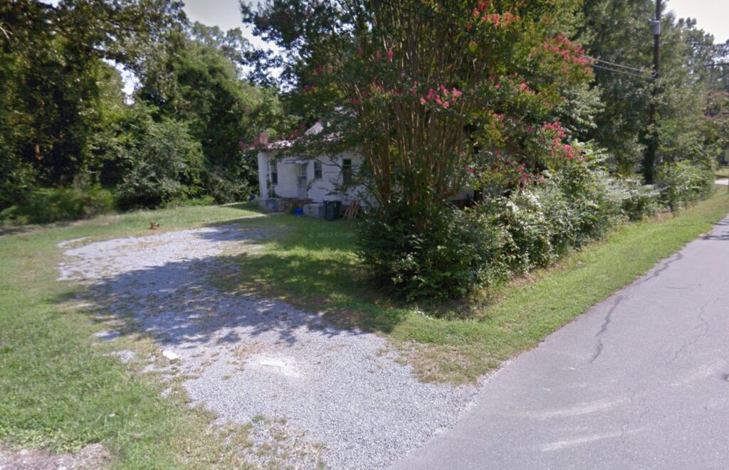 Photo of a small house with a gravel driveway hidden from the road by treees