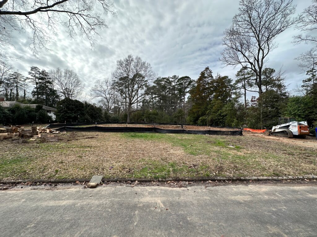 Photo of a grass lot with construction fencing and around a hole in the middle of it