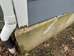 Photo of a home sitting on a foundation, with the edge of the home shifted off and separated from the foundation.