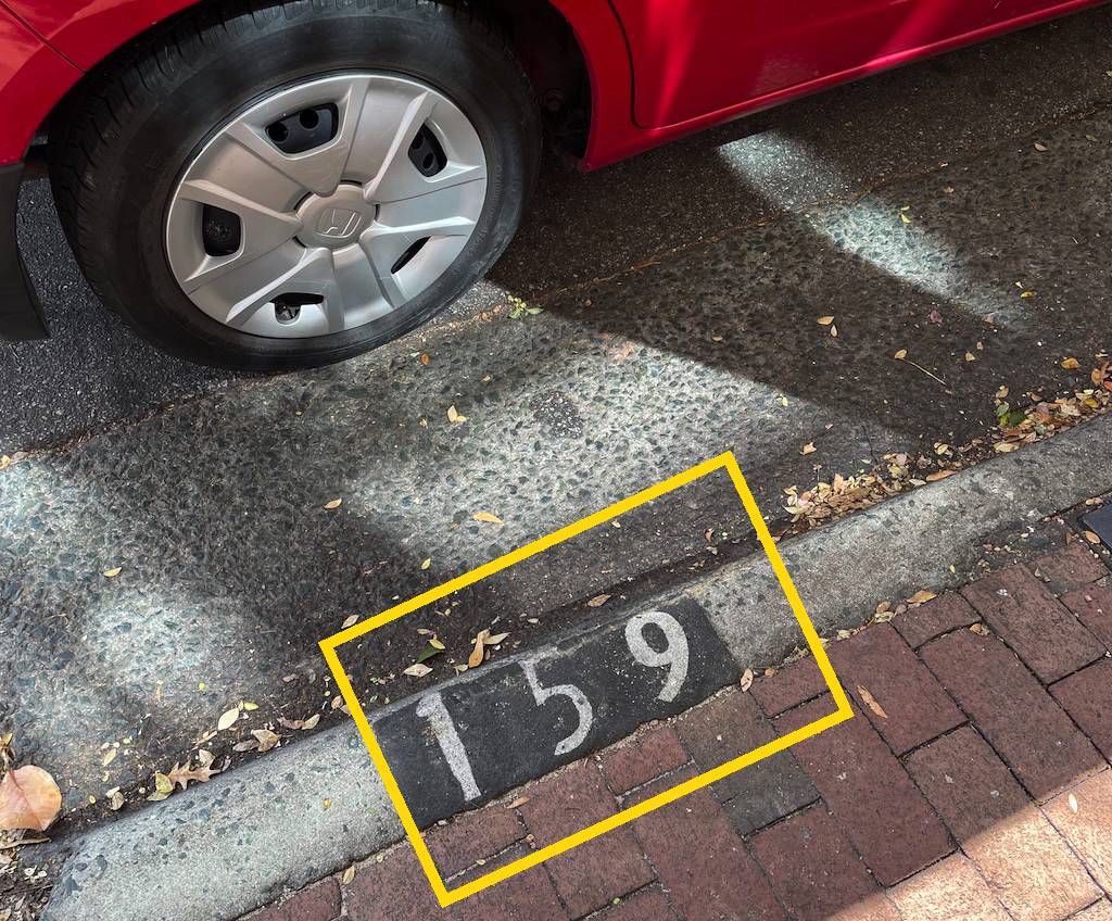 A photo of a car parked at a parking sport, with the number 159 painted o the curb