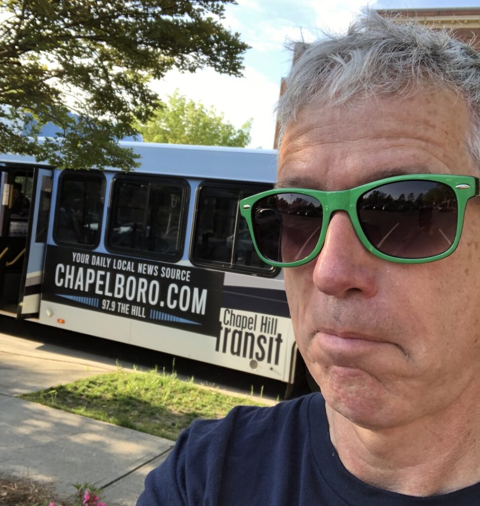 A man in sunglasses poses in front of a chapel hill transit bus in a selfie