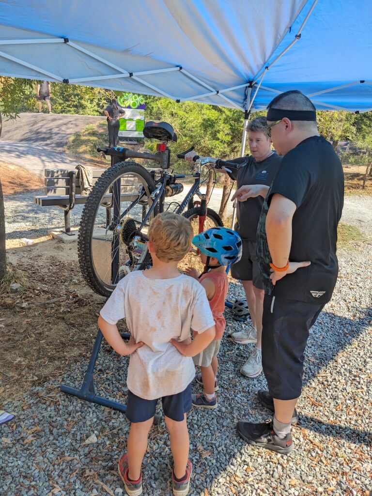 A mechanic works on a bike in a work stand as and adult and children look on