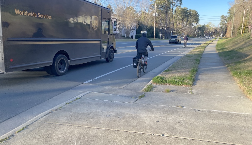 A bike lane and a sidewalk with to bike riders and a UPS truck