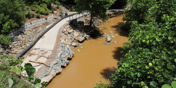 Drone image of Bolin Creek trail from what appears to be a couple hundred feet in the air, showing muddy water and damage to riprap along Bolin Creek Trail