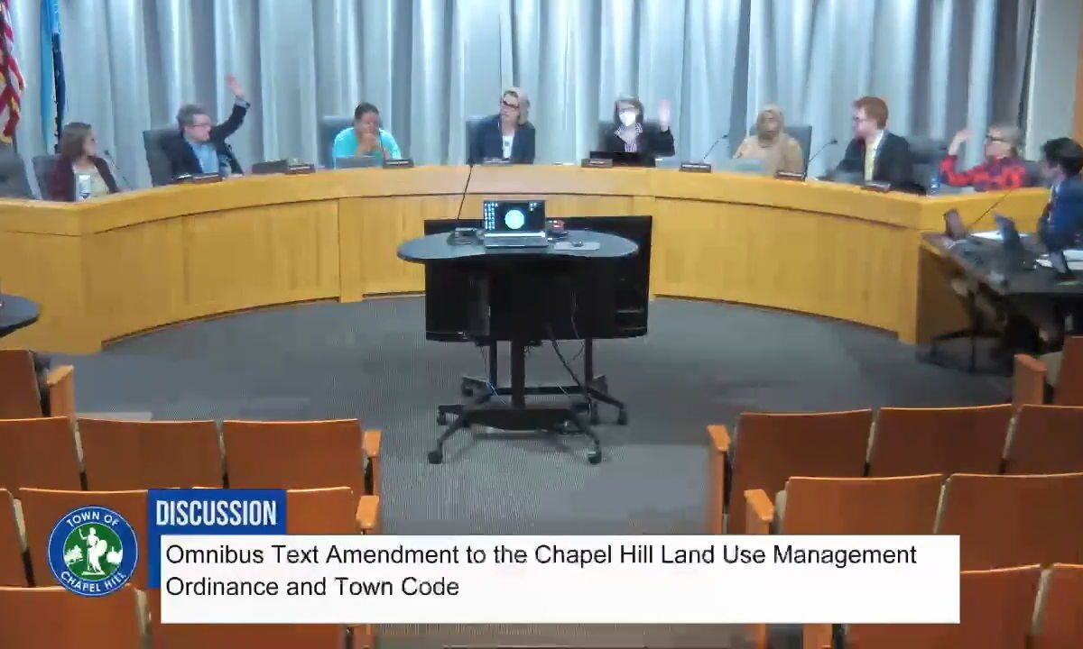 Screen capture of the Chapel Hill Town Council on November 19, 2025, showing seven council members and the mayor sitting behind the Dias. Three council members have their hands up. Text on the screen at the bottom states: "Discussion: Omnibus Text Amendment to the Chapel Hill Land Use Management Ordinance and Town Code"