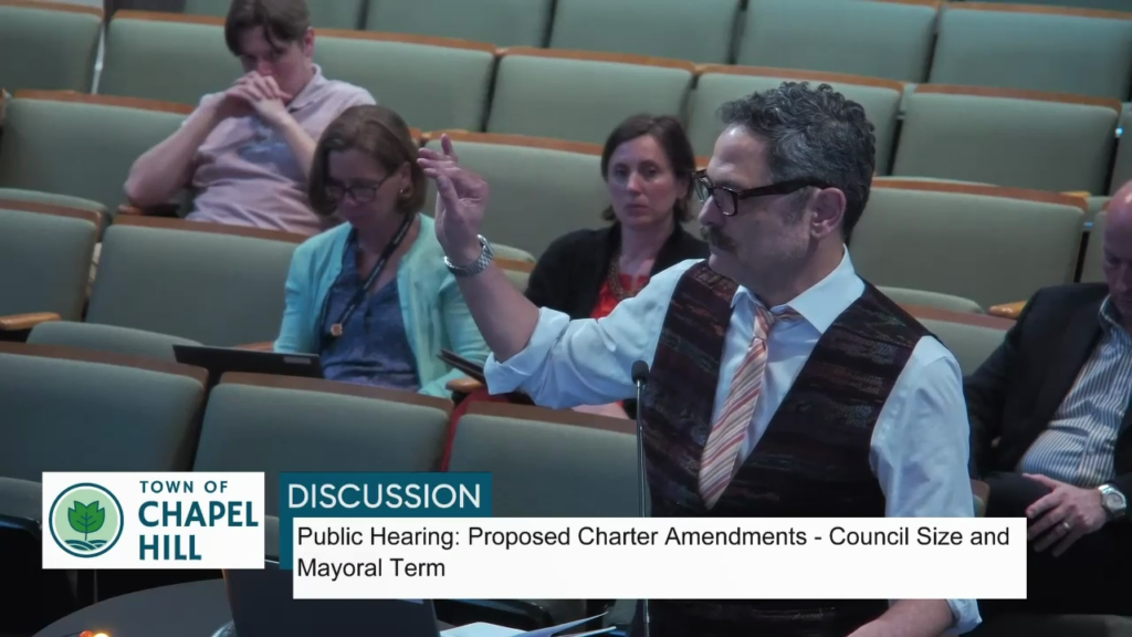 Video still of Mark Kleinschmidt speaking before Town Council. Text in the chyron underneath states Town of Chapel Hill: Discussion: Public Hearing: Proposed Charter Amendments - Council Size and Mayoral term